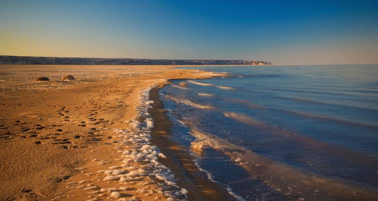 Une plage paisible avec des vagues douces et une falaise lointaine au coucher du soleil.