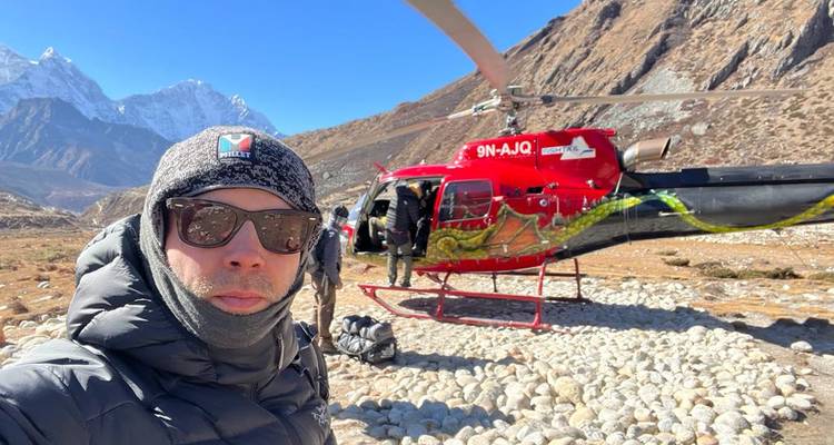 Des personnes en tenue d'hiver se tenant debout devant un hélicoptère dans un paysage montagneux.