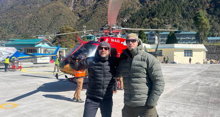 Deux personnes qui posent devant un hélicoptère sur un héliport.