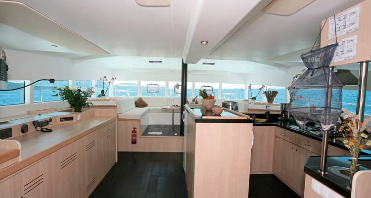 Salon moderne lumineux et coin cuisine à l'intérieur d'un catamaran à voile avec vues sur l'océan à travers des fenêtres panoramiques