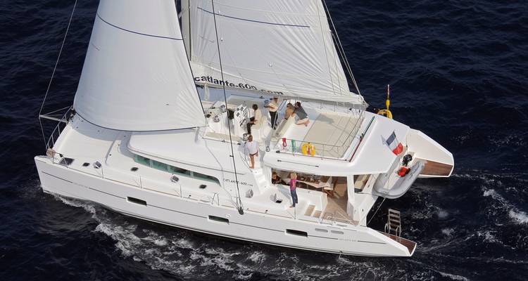 Catamaran de plaisance blanc fendant l'eau bleu foncé avec l'équipage se relaxant sur le pont soleil