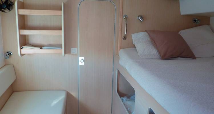 Cabine simple et confortable sur un yacht avec un lit surélevé, des étagères et des finitions en bois clair