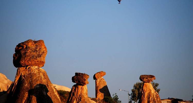 Vue du coucher de soleil sur des formations rocheuses avec une montgolfière dans le ciel.