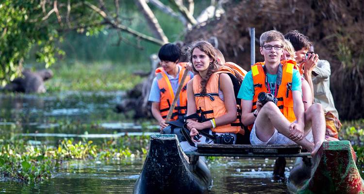 Young travellers wearing life jackets sit in a dugout canoe on a jungle waterway.