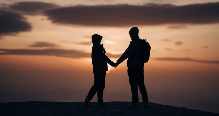 Silueta de dos personas tomadas de la mano al atardecer