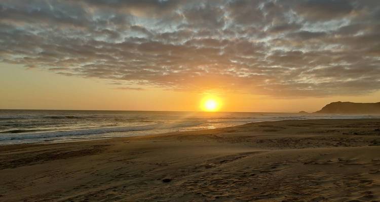 Coucher de soleil doré sur une plage tranquille avec des vagues douces et des formations nuageuses spectaculaires.