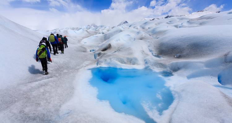 Un groupe de personnes faisant de la randonnée sur un glacier avec des formations de glace bleue.
