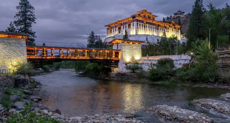 Vista panorámica de un Dzong bellamente iluminado junto a un río durante el crepúsculo.