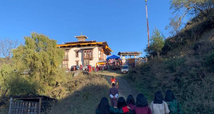 Un grupo de personas subiendo una colina hacia un edificio tradicional butanés.