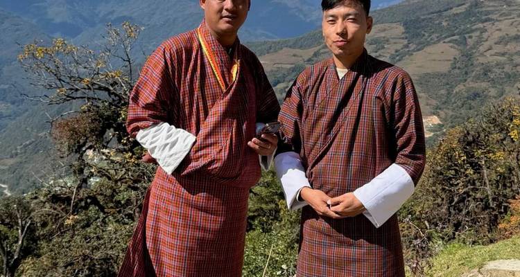 Dos hombres con vestimenta tradicional butanesa posando en un entorno montañoso.