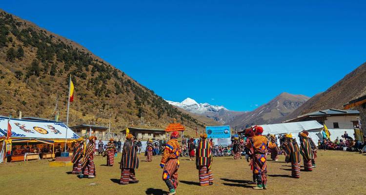 Festival tradicional butanés con participantes en atuendos coloridos en un entorno de valle.