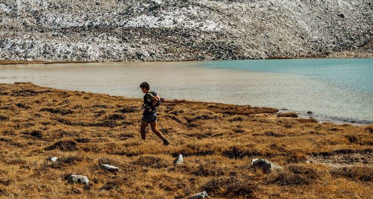 Persona corriendo junto a un lago alpino turquesa rodeado de terreno rocoso.