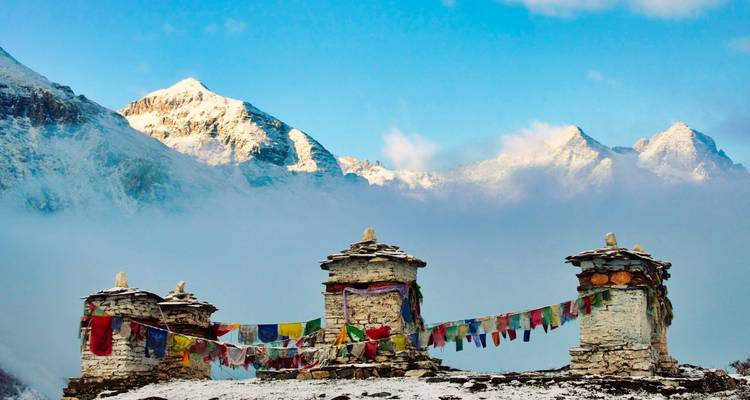 Les chortens aux sommets enneigés, drapés de drapeaux de prière colorés, s'élèvent devant les pics dramatiques de l'Himalaya et le brouillard matinal.