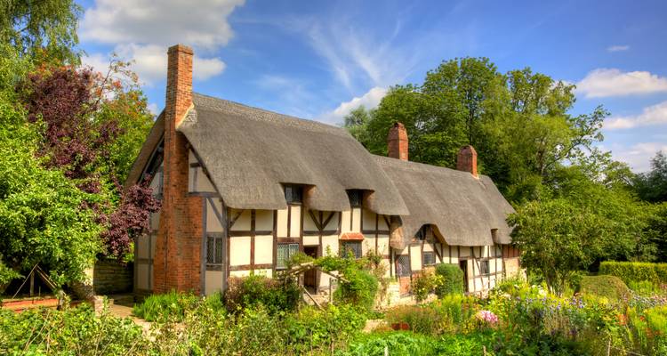 Charming cottage with thatched roof surrounded by gardens.