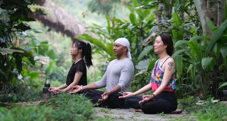 Trois personnes méditant en plein air près d'une végétation luxuriante.