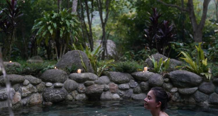 Femme se détendant dans un bassin thermal naturel dans un environnement forestier.