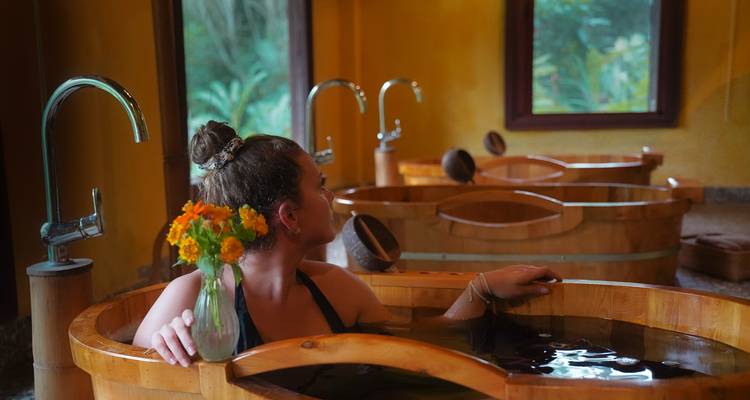 Femme dans un spa en bac de bois profitant d'une boisson et de la vue.