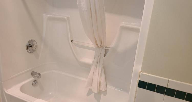 Primer plano de una bañera de baño limpia con una cortina de ducha parcialmente abierta.