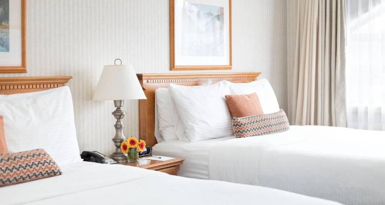 Habitación de hotel con dos camas, una lámpara y cojines decorativos en una mesa auxiliar.