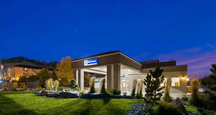 Vista exterior de un hotel bien iluminado al anochecer con jardines paisajísticos.