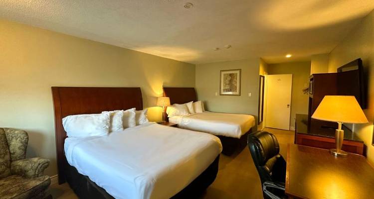 Hotelzimmer mit zwei großen Betten und warmer Beleuchtung, ein Schreibtisch ist vorhanden.