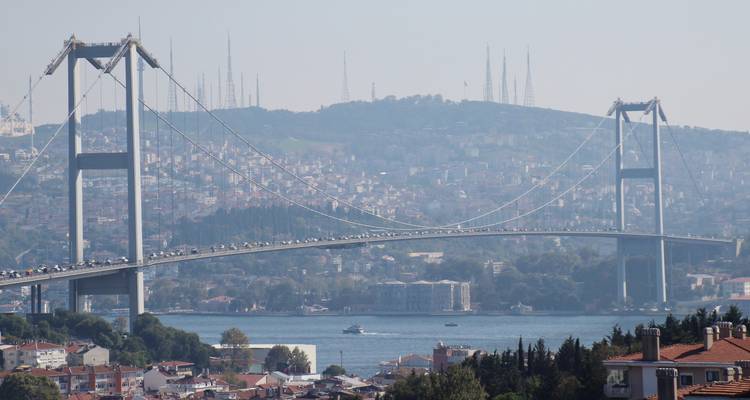 Pont suspendu enjambant un plan d'eau avec un paysage urbain en arrière-plan.