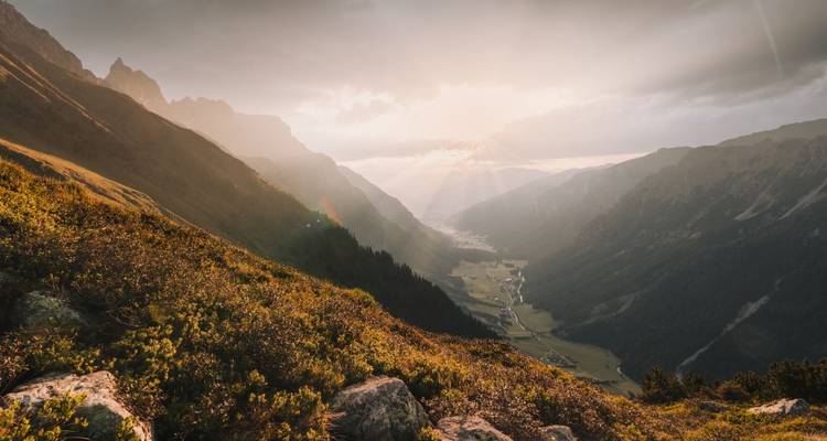 Rayons de soleil perçant les nuages au-dessus d'une vallée de montagne.
