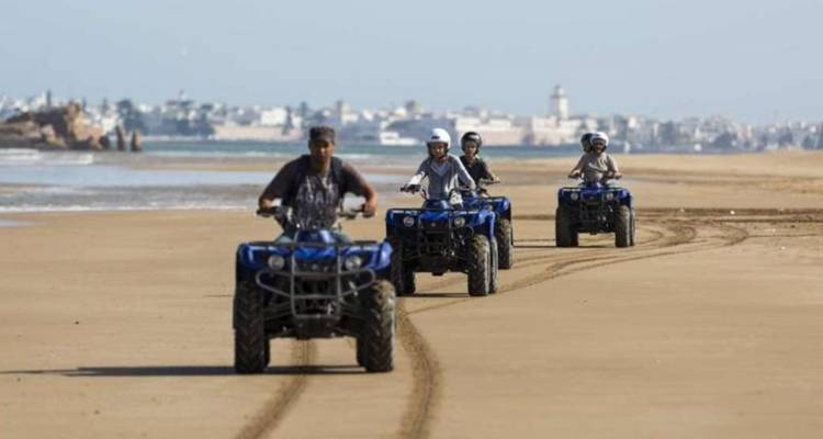 Menschen, die mit Quads einen sandigen Strand entlangfahren.