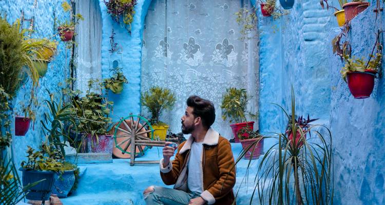 Un hombre sentado en un callejón azul vibrante adornado con plantas.