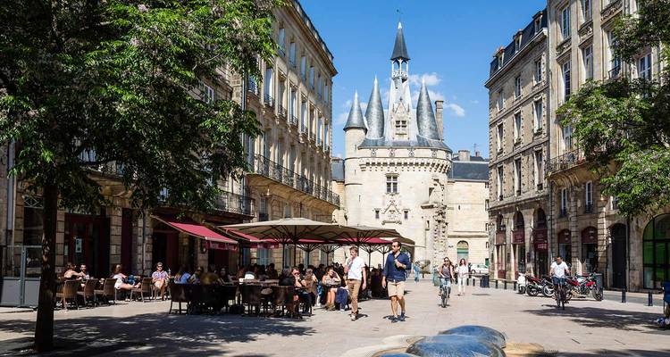 Bustling square in Bordeaux featuring medieval Porte Cailhau gate flanked by café terraces and historic buildings