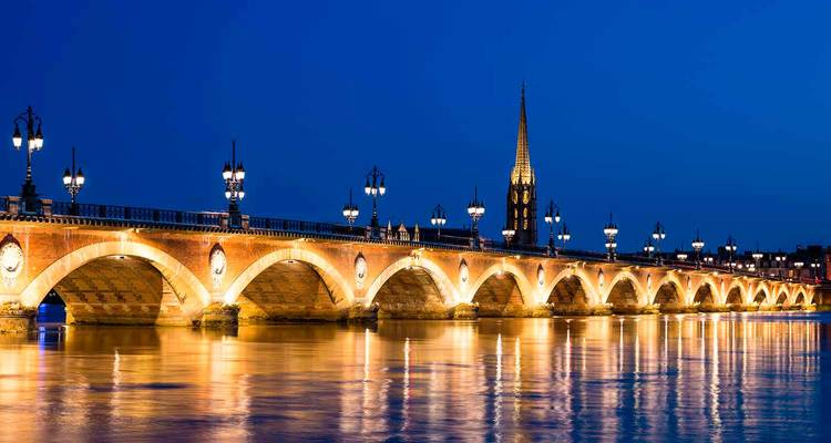 Vue nocturne du pont de Pierre de Bordeaux illuminé et reflété dans les eaux calmes de la Garonne