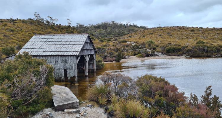 Une vue pittoresque d'un hangar à bateaux en bois rustique au bord d'un lac tranquille entouré de collines herbeuses.