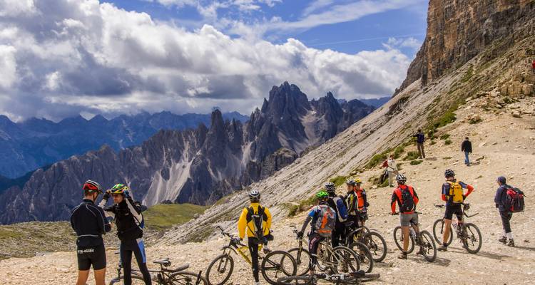 Des vététistes sur un sentier rocheux avec les Dolomites en arrière-plan.