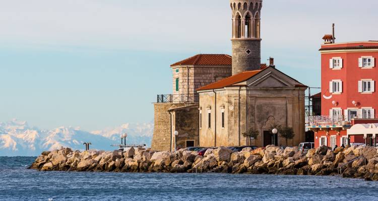 Iglesia histórica con vista al mar y montañas distantes.