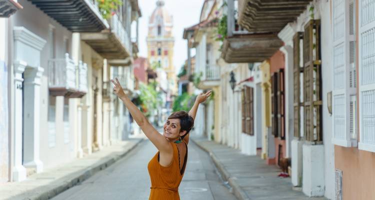Una mujer posando felizmente en una calle pintoresca bordeada de edificios coloniales.