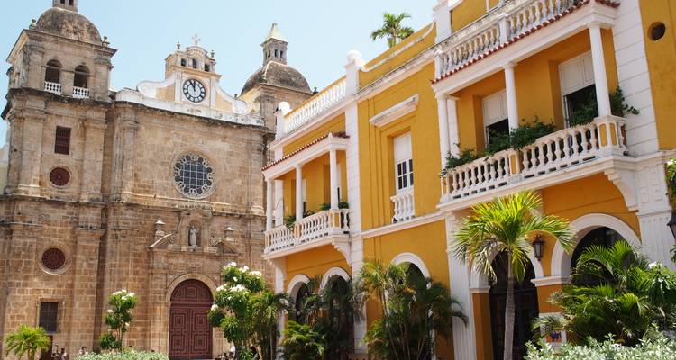 Una iglesia histórica y un edificio colonial amarillo vecino rodeados de palmeras.