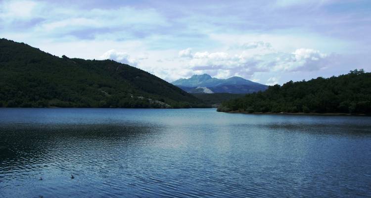 Un lac serein niché entre des collines verdoyantes sous un ciel lumineux.