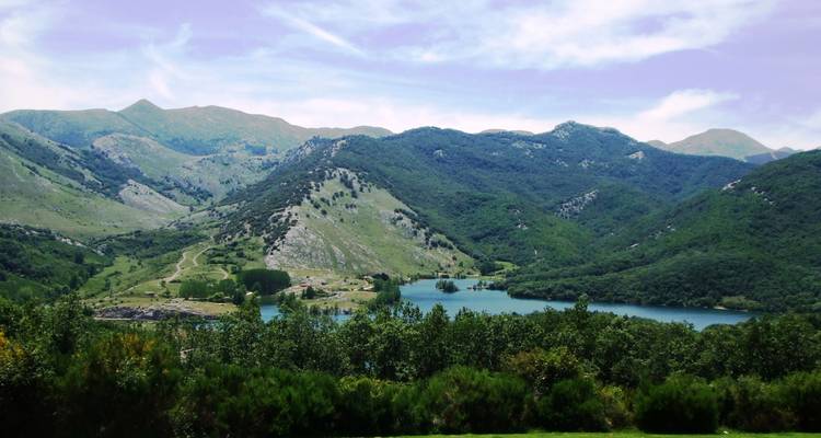 Vallée spacieuse avec un lac et des montagnes boisées en arrière-plan.