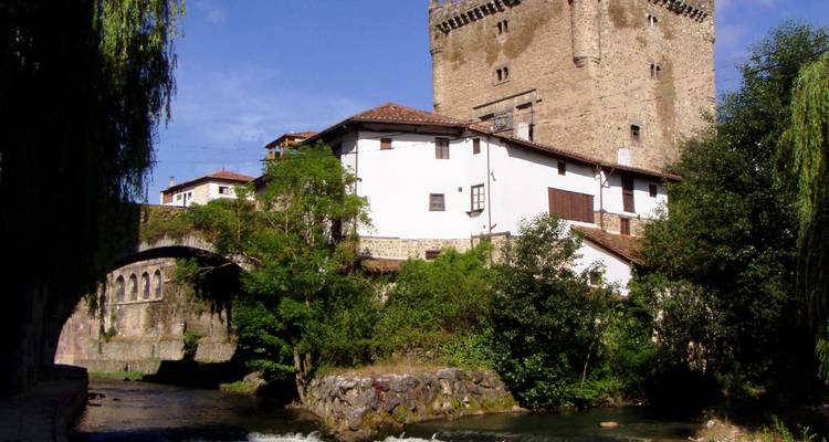 Bâtiment historique avec une tour au bord d'une rivière entouré de rangées d'arbres.
