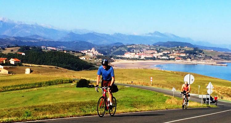 Des cyclistes roulant sur une route avec des vues panoramiques sur une plage et un village en arrière-plan.