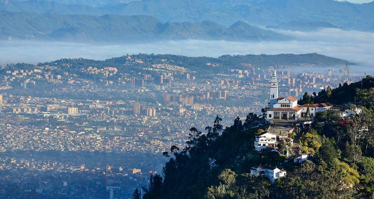 Panoramastadtansicht mit einer prominenten Kirche auf einem üppigen Hügel, die eine ausgedehnte Stadtlandschaft überblickt.