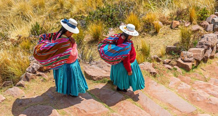 Zwei Frauen in traditioneller peruanischer Kleidung gehen einen Steinweg entlang.