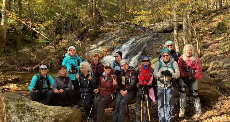 Grupo de personas posando frente a una cascada en un bosque.