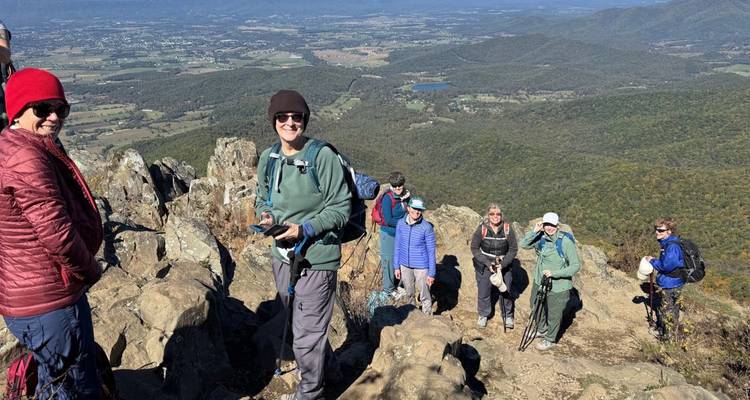 Excursionistas en la cima de una cumbre rocosa con vista del valle abajo.