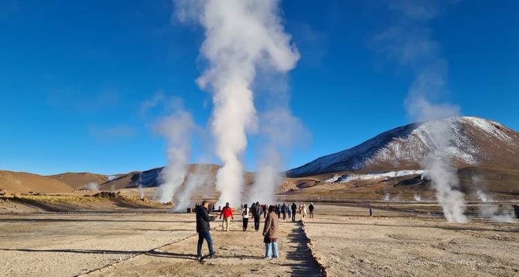 Des touristes explorant un champ de geysers avec de la vapeur qui s'élève autour d'eux.