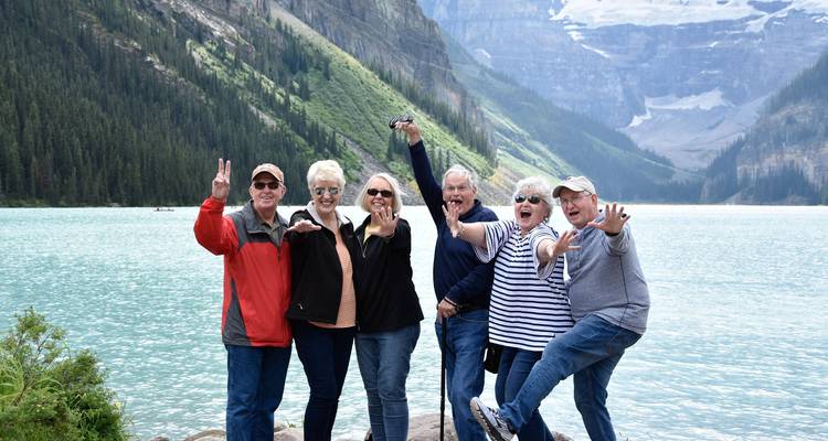 Grupo de personas posando junto a un lago con montañas al fondo.