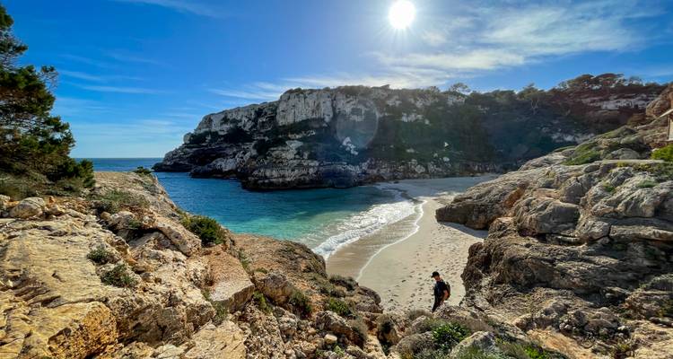 Une personne marchant sur une plage de sable avec des falaises rocheuses et un ciel bleu clair.
