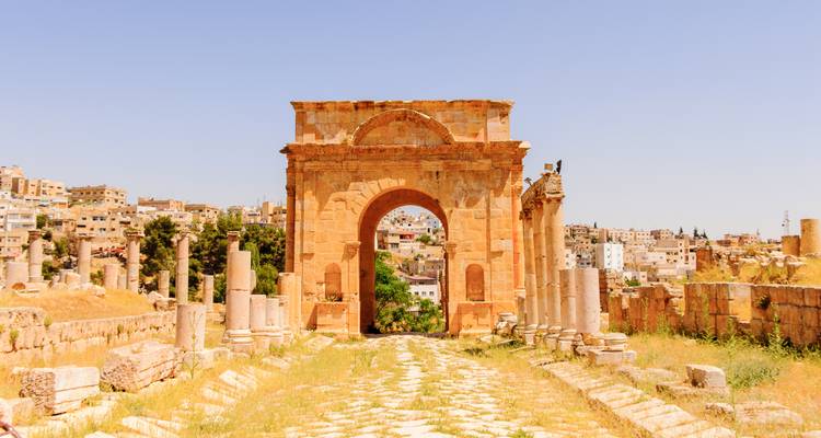 L'Arc d'Hadrien et les ruines à colonnades de Jerash encadrées par la chaude lumière de midi.