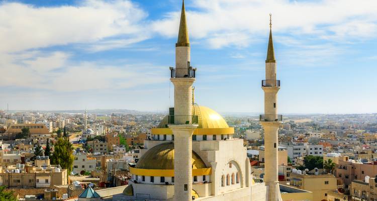 Mosquée au dôme doré avec deux minarets jumeaux s'élevant au-dessus du paysage urbain sous des nuages épars.