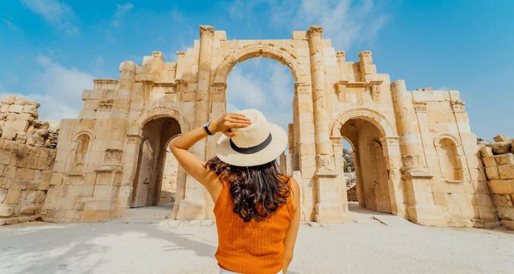 Frau mit Hut bewundert monumentalen Bogen der antiken Jerash-Ruinen an einem hellen Tag.